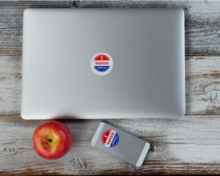 Laptop and cell phone sitting on table each with I Voted stickers on them